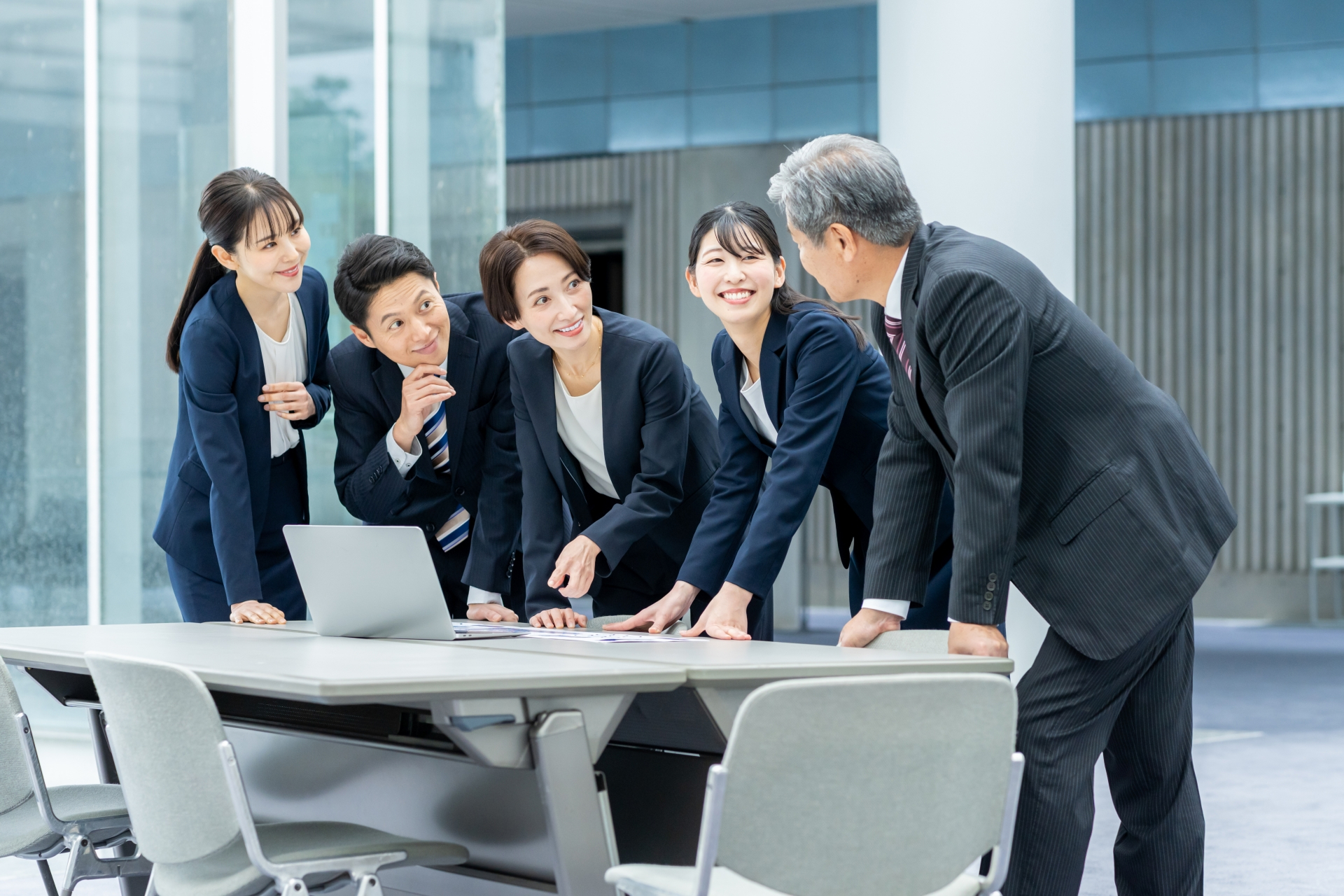 オフィスで机と椅子の前でスーツを着たビジネスパーソン5人による楽しそうな会話