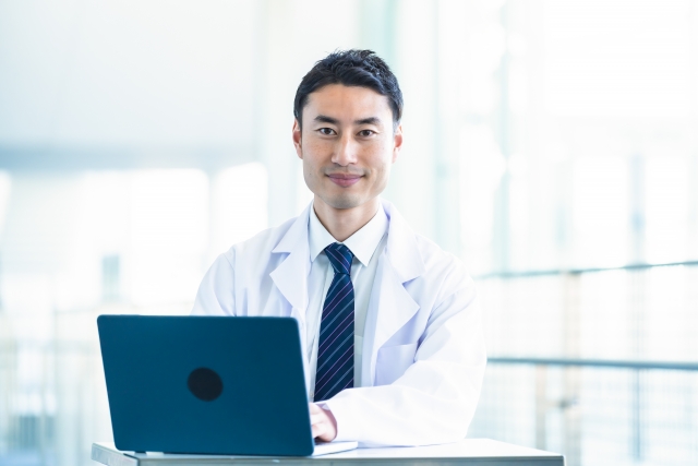 病院内でノートパソコン前で座る白衣を着る男性